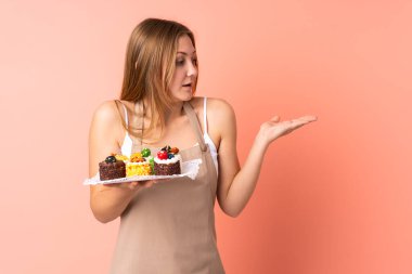 Pastacı Ukraynalı şef pembe arka planda izole edilmiş bir kek tutuyor.