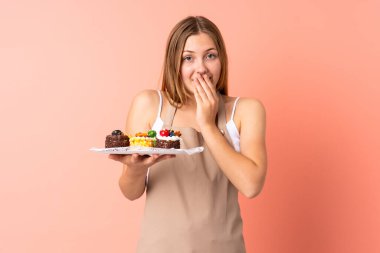 Ukraynalı aşçı pembe arka planda yüzünde sürpriz bir ifadeyle izole edilmiş bir kek tutuyor.