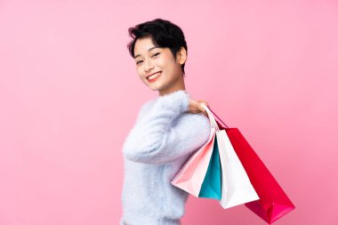 Soyutlanmış pembe arka planı olan genç bir Asyalı kız alışveriş torbaları tutuyor ve gülümsüyor.