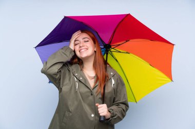 Kızıl saçlı genç kız mavi arka planda şemsiye tutuyor ve gülüyor.