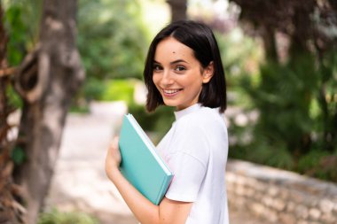 Dışarıda elinde defterler tutan genç ve mutlu bir öğrenci kadın.