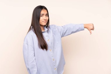 Bej arka planda izole edilmiş genç Hintli kadın, olumsuz ifade ile baş parmağını aşağı gösteriyor.