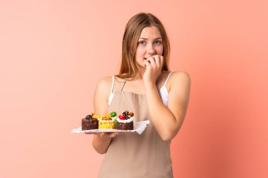 Ukraynalı aşçı pembe arka planda izole edilmiş kek tutuyor. Gergin ve korkmuş.