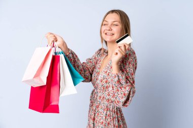 Genç Ukraynalı kız mavi arka planda izole edilmiş. Elinde alışveriş torbaları ve bir kredi kartı var.