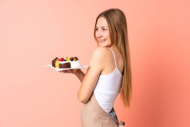 Ukraynalı aşçı pembe arka planda izole edilmiş bir kek tutuyor.