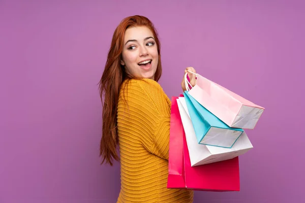 Pelirroja Adolescente Chica Sobre Aislado Púrpura Fondo Sosteniendo Bolsas Compras —  Fotos de Stock