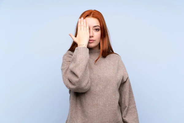 Ruiva Adolescente Com Suéter Sobre Fundo Azul Isolado Cobrindo Olho — Fotografia de Stock