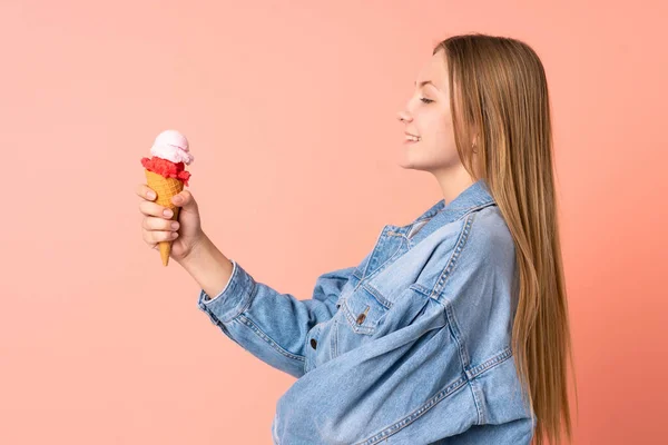 Teenager Ukrainian girl with a cornet ice cream isolated on pink background with happy expression