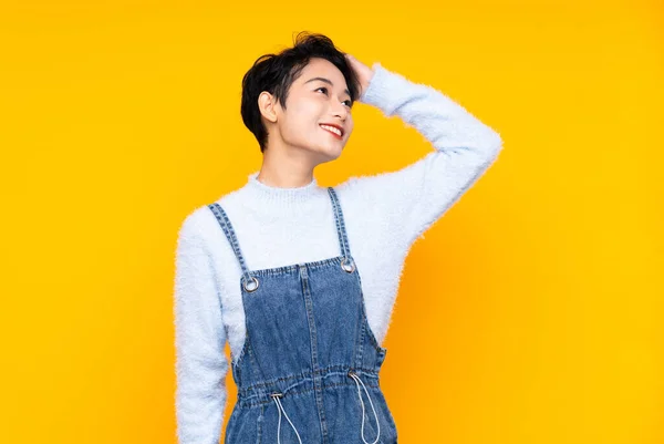 Young Asian girl in overalls over isolated yellow background laughing