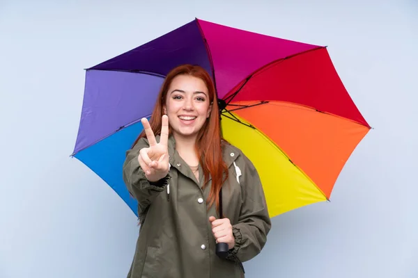 Pelirroja Adolescente Sosteniendo Paraguas Sobre Fondo Azul Aislado Sonriendo Mostrando —  Fotos de Stock