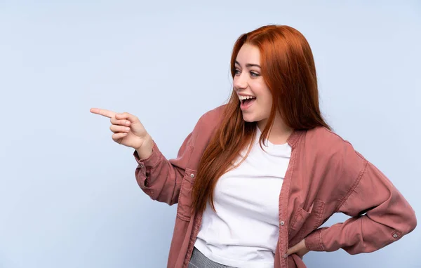 Ruiva Adolescente Sobre Fundo Azul Isolado Apontando Dedo Para Lado — Fotografia de Stock