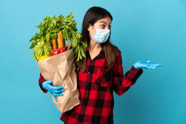 Young caucasian with vegetables and mask isolated on blue background with surprise facial expression