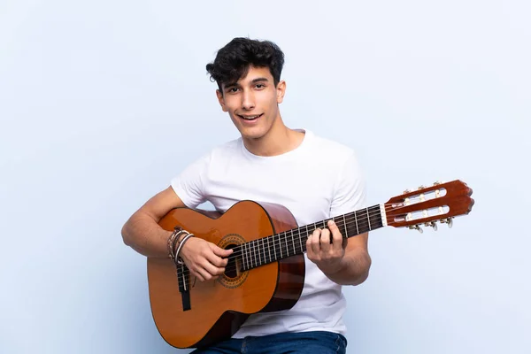 Jonge Argentijnse Man Met Gitaar Geïsoleerde Blauwe Achtergrond Wijzend Een — Stockfoto