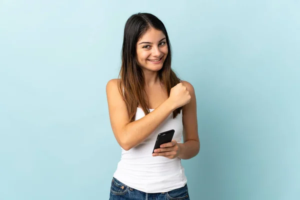 Молода Біла Жінка Використовує Мобільний Телефон Ізольовано Синьому Фоні Відзначаючи — стокове фото