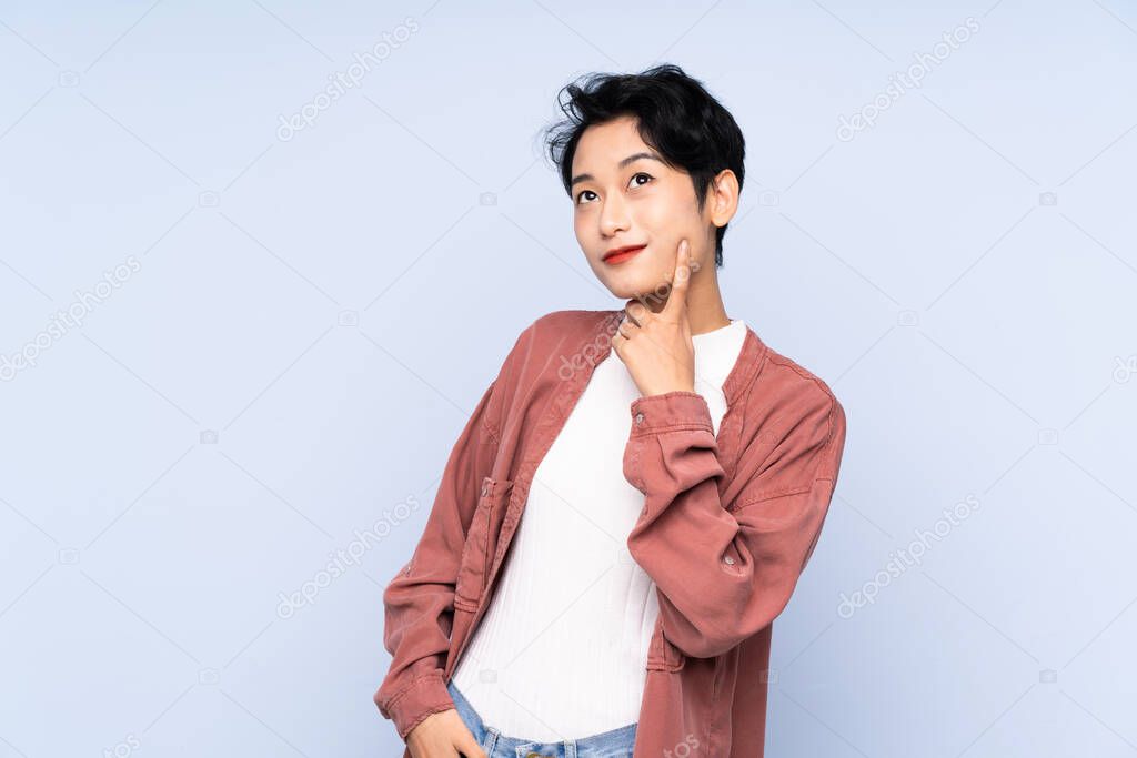 Young Asian girl over isolated blue background thinking an idea while looking up