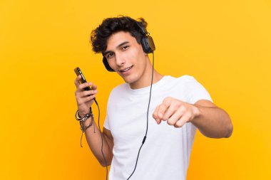 Arjantinli genç adam, izole edilmiş sarı bir duvarın üzerinde gezici bir araçla müzik dinliyor.