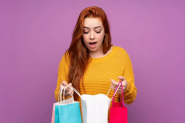 赤毛ティーン女の子上の隔離された紫色の背景を保持ショッピングバッグと見る上にそれ — ストック写真
