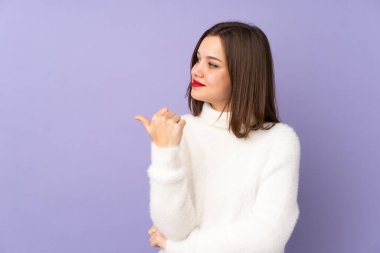 Mor arka planda izole edilmiş genç bir kız bir ürünü sunmak için kenarı işaret ediyor.