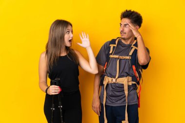 Sarı arka planda büyük bir sırt çantası olan genç dağcı çift şaşırmış ve şok olmuş bir yüz ifadesine sahipler.