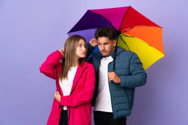 Mavi arka planda şemsiye tutan çift kafalarını kaşırken şüpheye düşüyor.