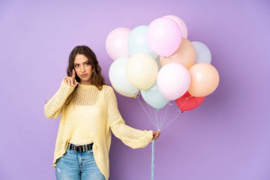 Mor arka planda izole edilmiş balonları yakalayan genç bir kadın şeffaf ekrana dokunuyor.