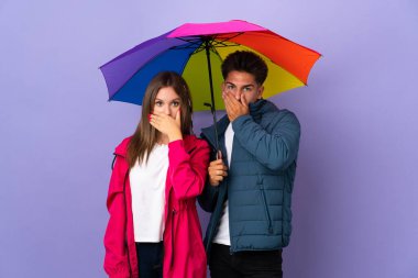 Mavi arka planda şemsiye tutan çift uygunsuz bir şey söylediği için ağızlarını elleriyle kapatıyor.