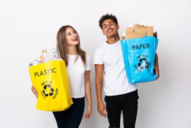 Beyaz arka planda izole edilmiş plastik ve kağıt dolu bir çanta taşıyan genç çift gülüyor.