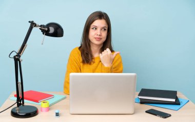 Evinde okuyan öğrenci kız mavi arka planda izole edilmiş bir şekilde bir ürünü sunmak için kenarı işaret ediyor.