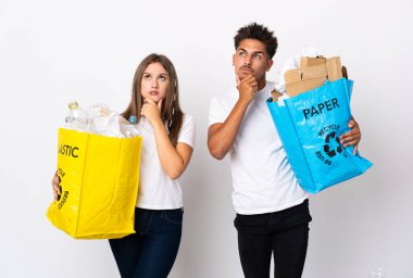 Plastik ve kağıt dolu bir çanta taşıyan genç çift beyaz arka planda kuşkuları olmadan izole edilmiş.