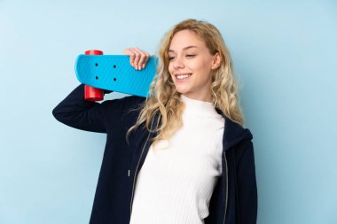 Genç sarışın kadın mavi arka planda tek başına paten kayıyor.