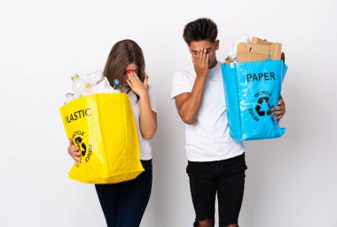 Plastik ve kağıt dolu bir çanta taşıyan genç bir çift yorgun ve hasta bir ifadeyle beyaz arka planda izole edilmiş.