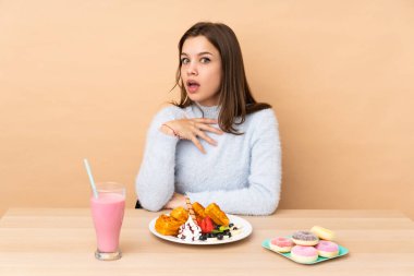 Bej arka planda izole edilmiş waffle yiyen genç kız sağa bakarken şaşırmış ve şok olmuştu.