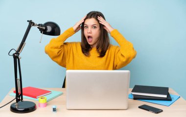 Evinde okuyan öğrenci kız mavi arka planda, sürpriz bir ifadeyle izole edilmiş.