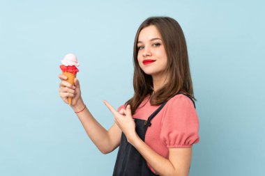 Kornet dondurması tutan genç kız mavi arka planda izole edilmiş ve onu işaret ediyor.