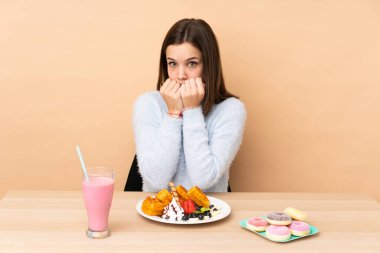 Bej arka planda izole edilmiş waffle yiyen genç kız gergin ve elleri ağıza vermeye korkuyor.