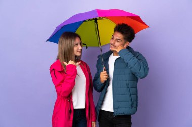 Mavi arka planda şemsiyesi olan çift telefon jesti yapıyor. Bana geri dönüş işareti ver.