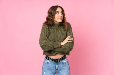 Soyutlanmış pembe arka planı olan genç bir kadın omuzlarını kaldırırken şüphe jesti yapıyor.