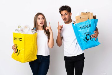 Beyaz arka planda izole edilmiş plastik ve kâğıt dolu bir çanta taşıyan genç çift, bir fikir öne sürüp,