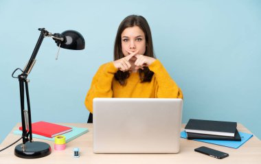 Öğrenci kız evinde çalışıyor. Mavi arka planda izole edilmiş. Sessizlik işareti gösteriyor.