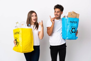 Beyaz arka planda izole edilmiş plastik ve kağıt dolu bir çanta tutan genç çift, çözümü fark etmek için parmağını kaldırıyor.