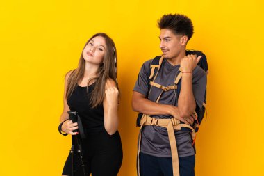 Sarı arka planda büyük bir sırt çantası olan genç dağcı çift zaferi kutluyor.