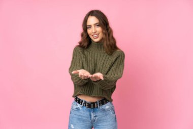 İzole edilmiş pembe arka planı olan genç bir kadın bir ilan vermek için fotokopi cihazını avucunun içinde tutuyor.
