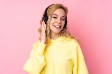 Pembe arka planda izole edilmiş sweatshirt giyen genç sarışın kadın müzik dinliyor.