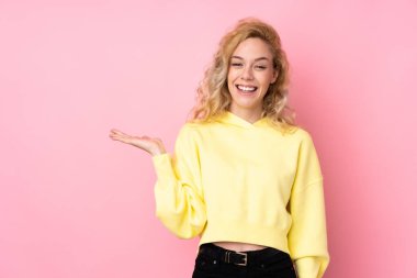 Pembe arka planda izole edilmiş eşofman üstü giyen genç sarışın kadın bir ilan vermek için avucunda hayali bir fotokopi makinesi tutuyor.