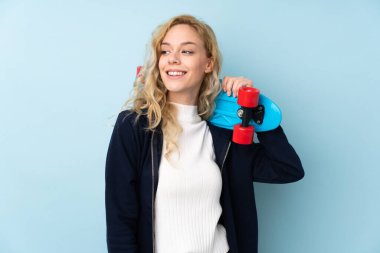 Mavi arka planda izole edilmiş genç sarışın kadın mutlu bir ifadeyle paten kayıyor.