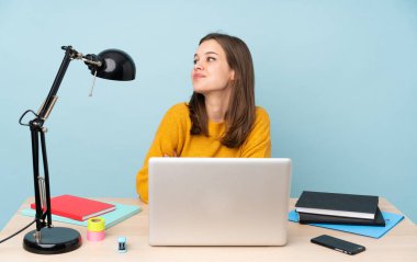 Evinde okuyan öğrenci kız mavi arka planda mutlu ve gülümsüyor.