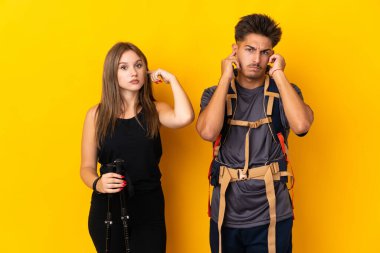 Sarı arka planda izole edilmiş büyük sırt çantalı genç dağcı çift iki kulağını da elleriyle kapatıyor.