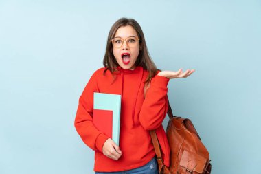 Mavi arka planda izole edilmiş kitapları tutan öğrenci kız mutsuz ve hayal kırıklığına uğramış.