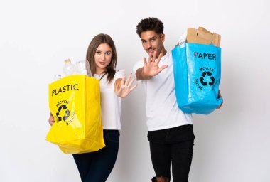 Beyaz arka planda plastik ve kağıt dolu bir çanta taşıyan genç çift, parmaklarıyla beşi sayıyor.