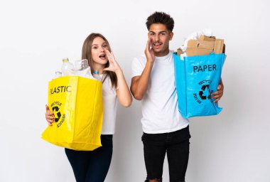 Beyaz arka planda ağzı açık bağıran plastik ve kağıt dolu bir çanta tutan genç çift.